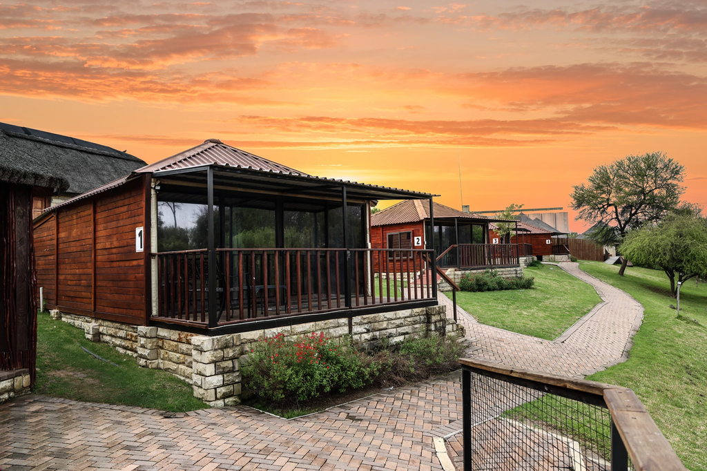 Wooden chalets with glazed verandas beside a brick pathway curving through the lawns at sunset.