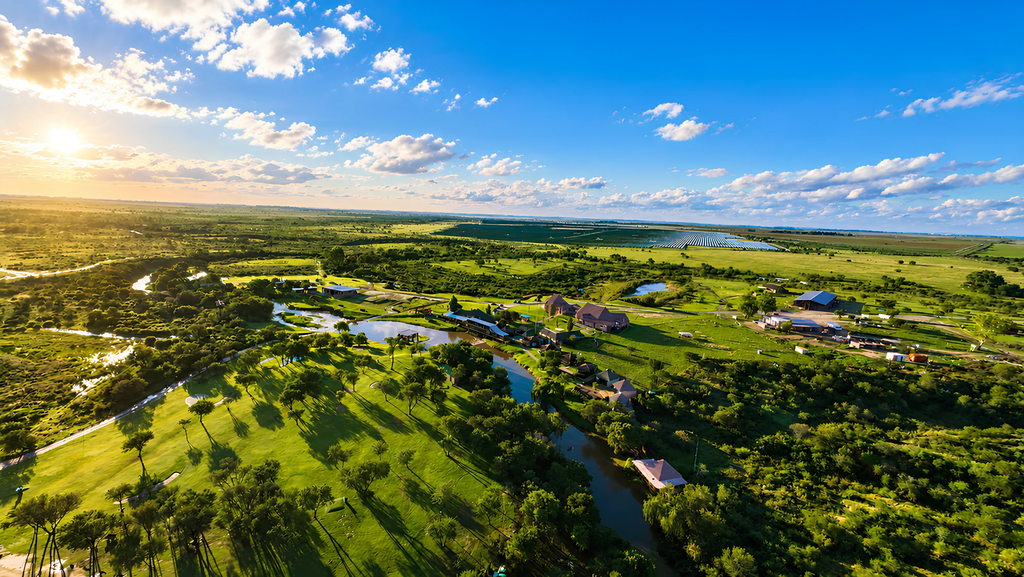 The ranch buildings set among trees and open Free State grassland, seen from the air.