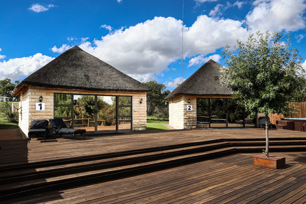 Loungers and seating on the wide timber deck outside two thatched stone units.