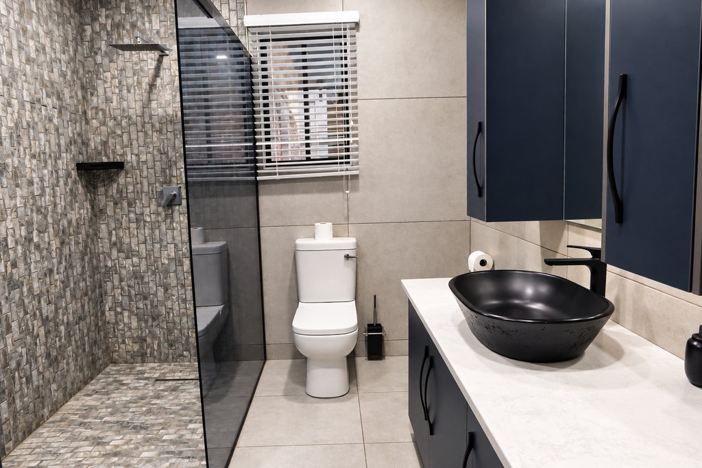 A Family Room bathroom with a dark vanity and basin, a toilet and a large walk-in shower behind a glass screen.