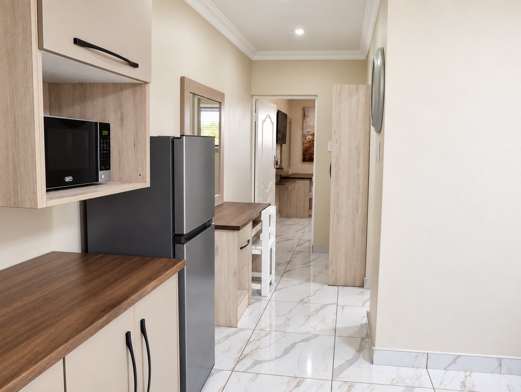 The kitchen and passage of a Family Room, with the microwave and fridge/freezer beside the desk nook and the way through to the bedroom.