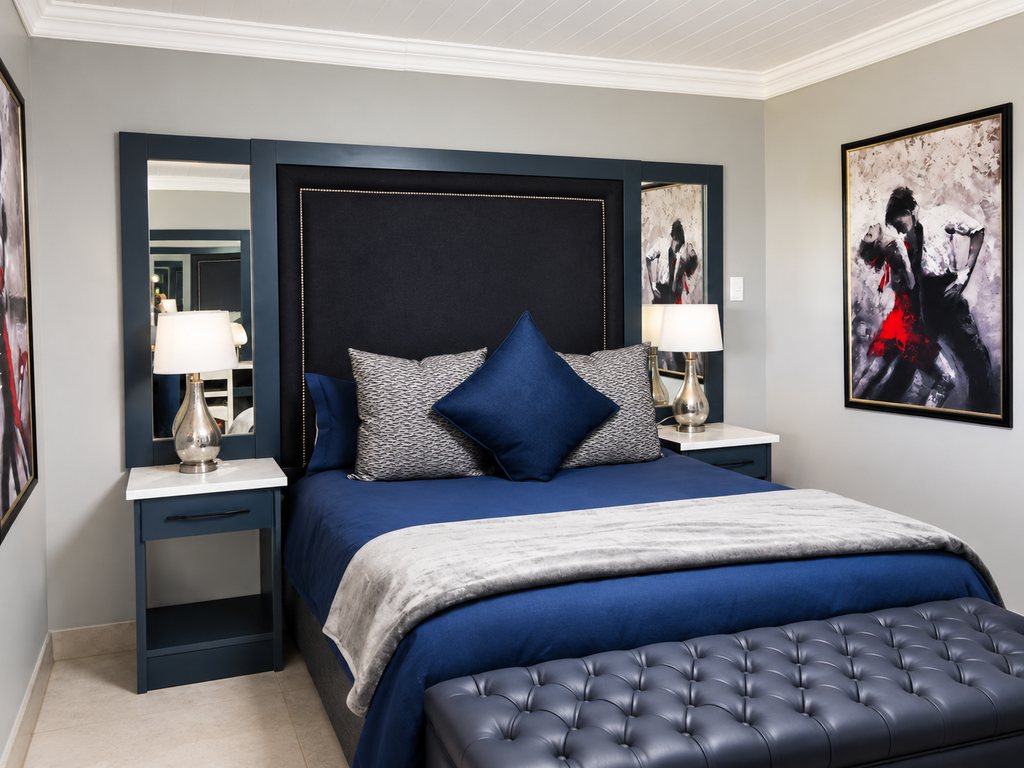 The main bedroom seen from the side, showing the queen bed, bedside tables and a buttoned bench at the foot of the bed.