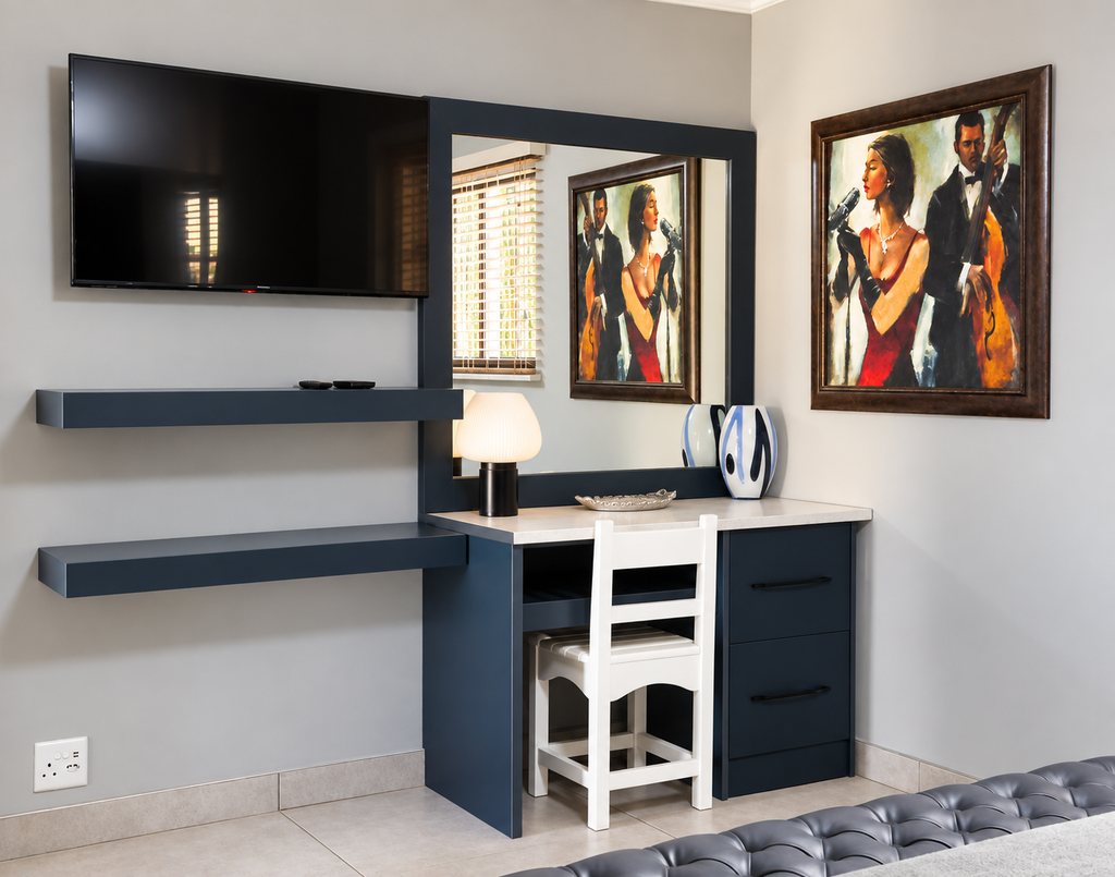 The living corner of a Family Room, with a wall-mounted television, floating shelves and a desk with a mirror.