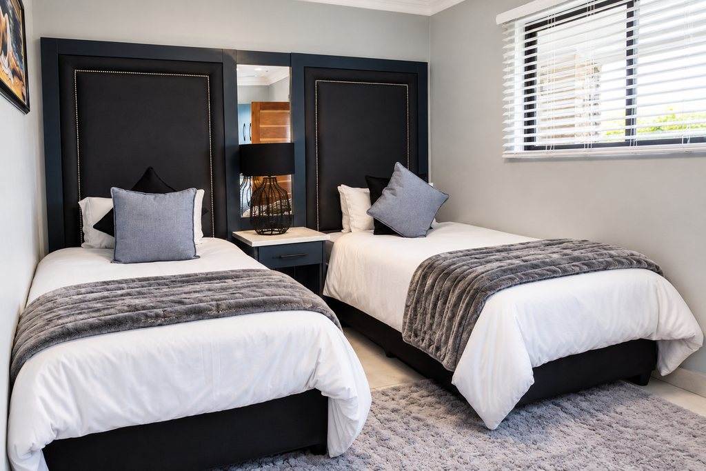 The second bedroom of a Family Room, with two single beds, tall navy headboards and a window with louvre blinds.