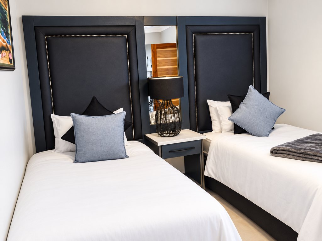 The two single beds in a Family Room second bedroom seen close, with navy headboards, a mirror panel and a bedside lamp.