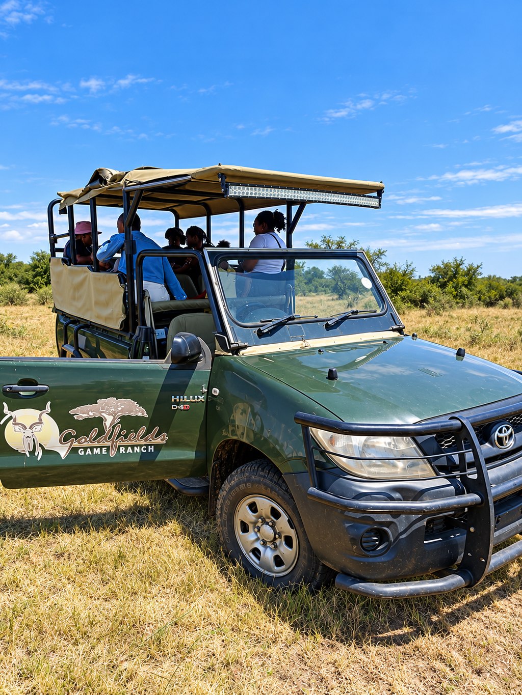 Guests seated in the open Goldfields Game Ranch game-viewing vehicle in the grassland.