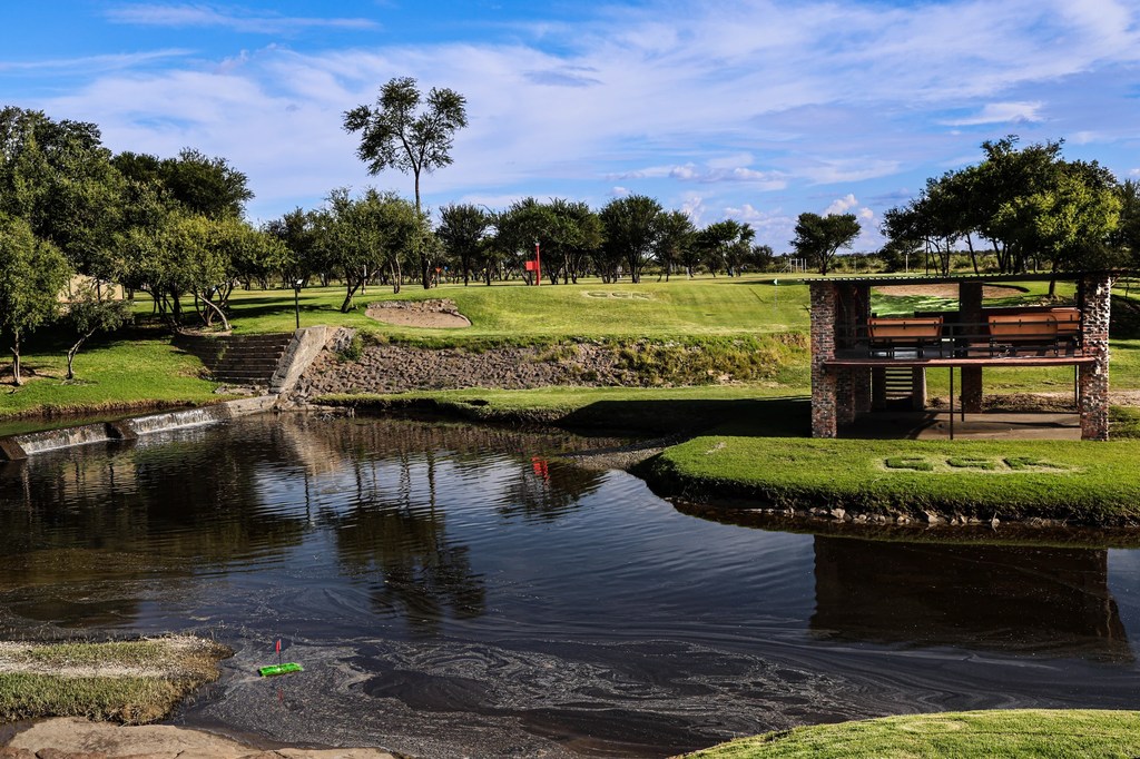 The Goldfields golf course beside the water, with a brick halfway shelter above the weir and mown fairways beyond.