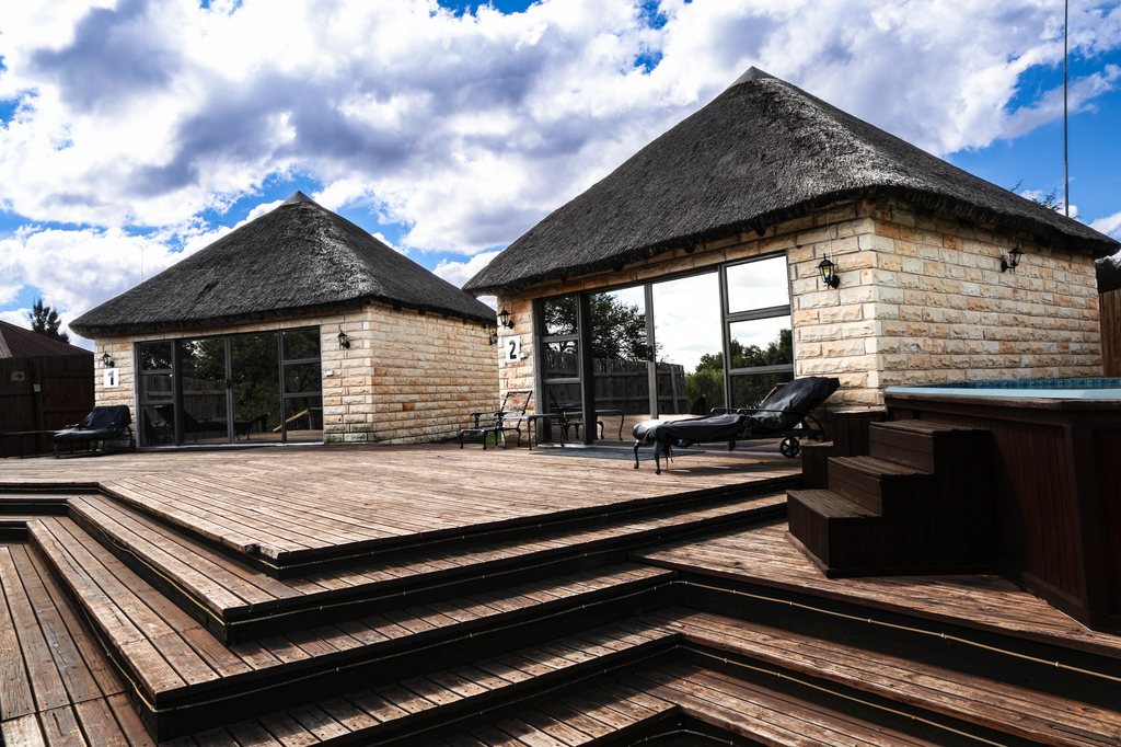 Two thatched stone units opening onto a wide timber deck beside the pool.