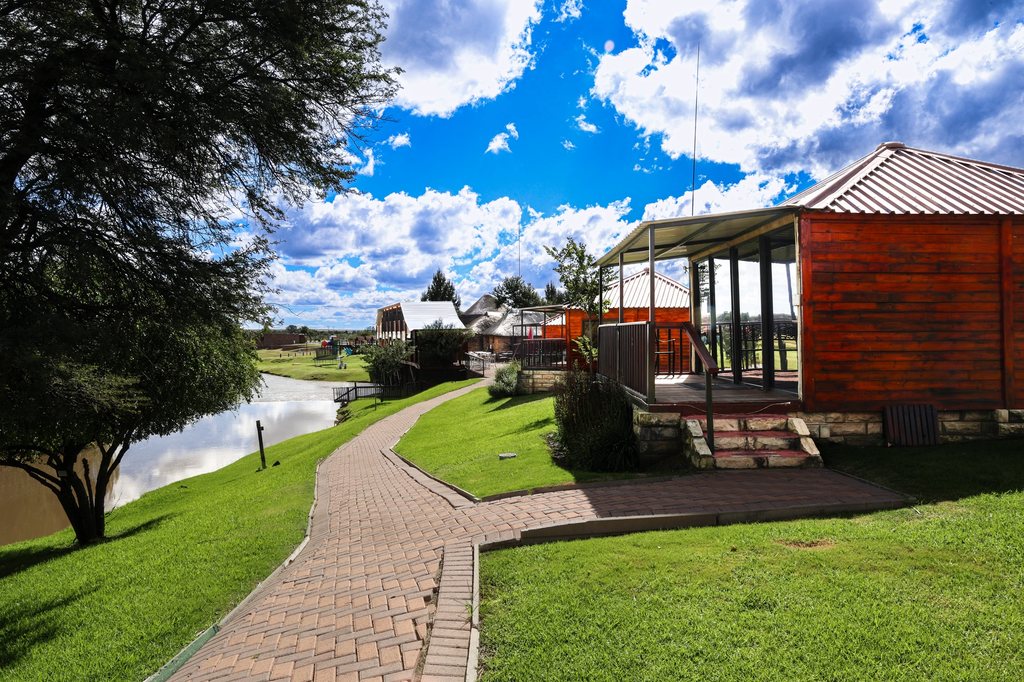 A riverside timber chalet at Goldfields, with a brick pathway following the water.