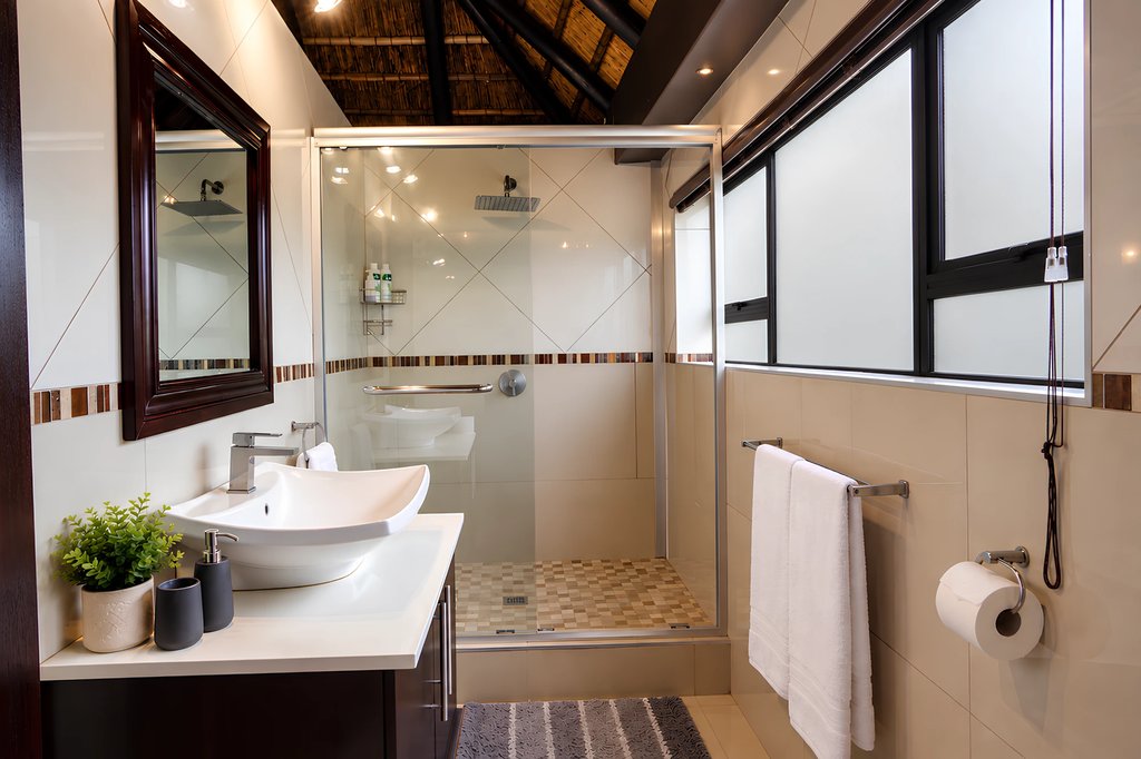 The Honeymoon Suite bathroom, with a basin, mirror and glass shower with a rain head.