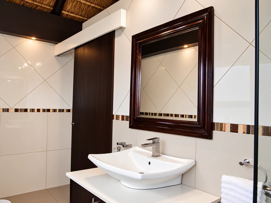 A basin beneath a dark timber-framed mirror in the Honeymoon Suite bathroom, with the thatched roof above.