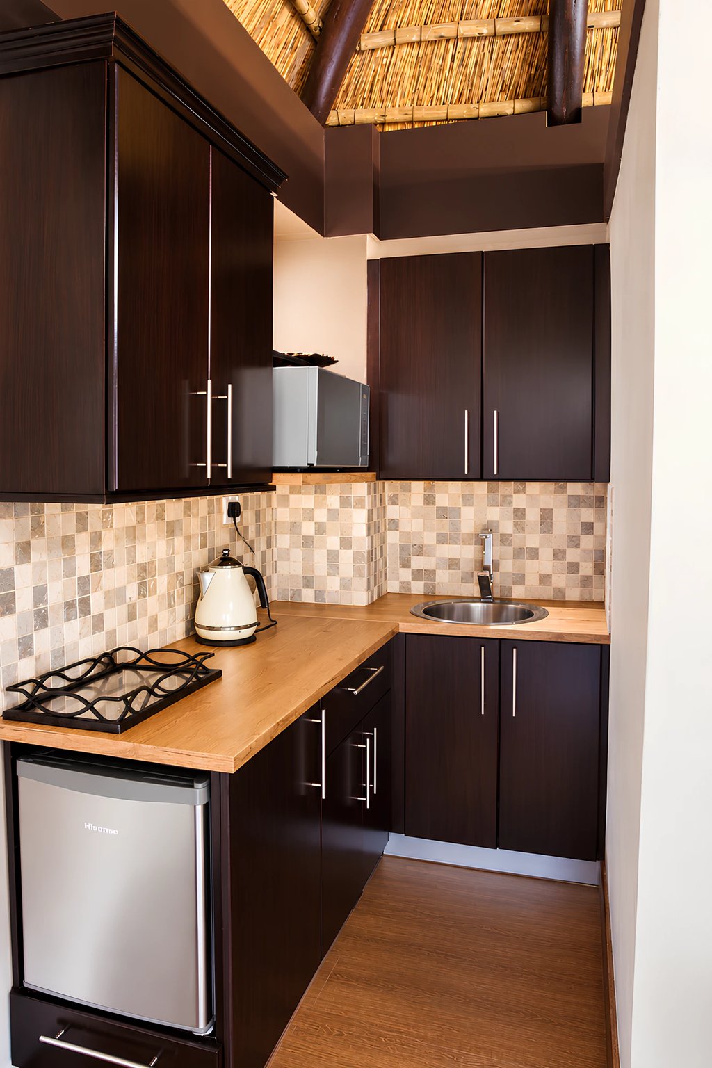 The kitchen in the Honeymoon Suite, with dark timber units, a timber worktop, microwave, kettle and bar fridge.
