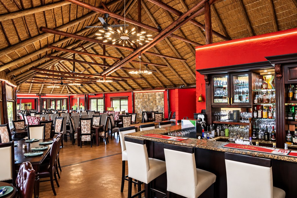 The dining room at the Goldfields restaurant, with laid tables and the bar beneath a thatched roof.