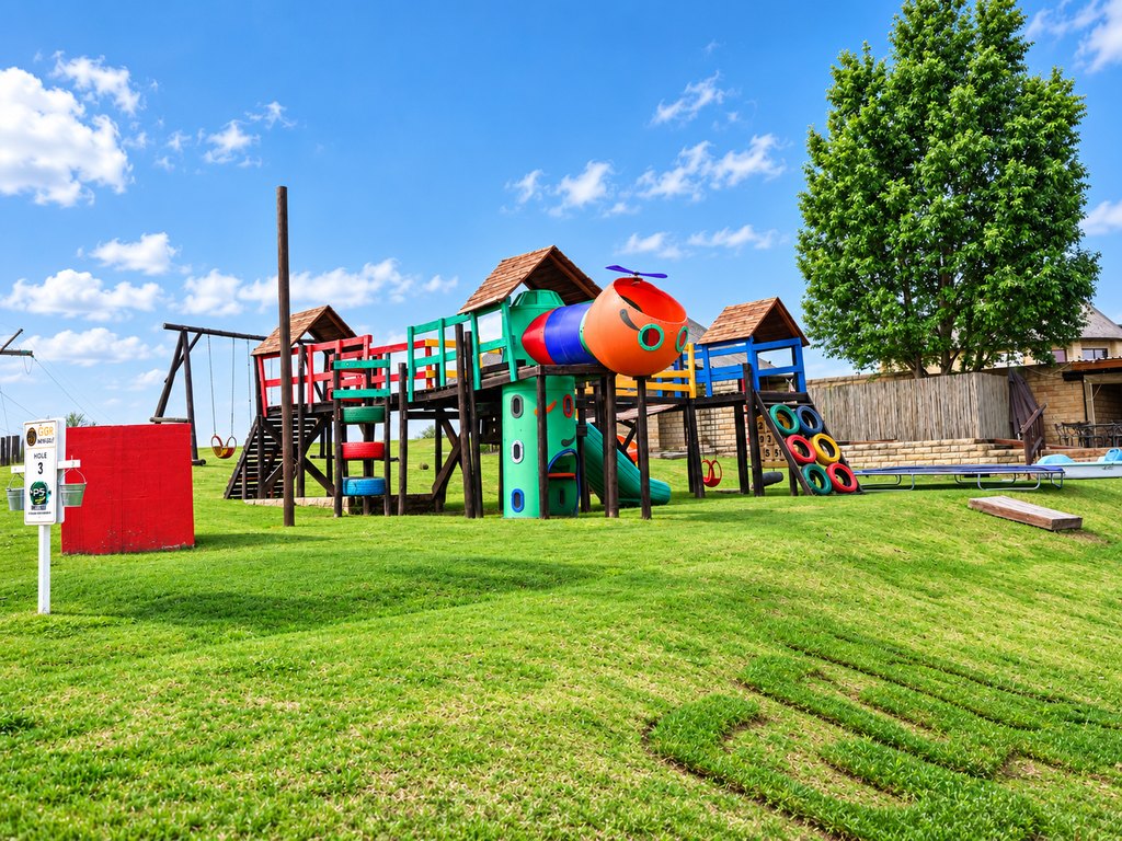 The children's outdoor play area at Goldfields, with a wooden climbing frame, slides and swings on the lawn.