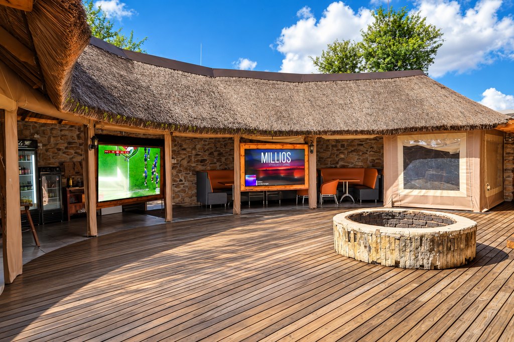 A large screen showing rugby beside booth seating and the fire pit on the deck at Goldfields.