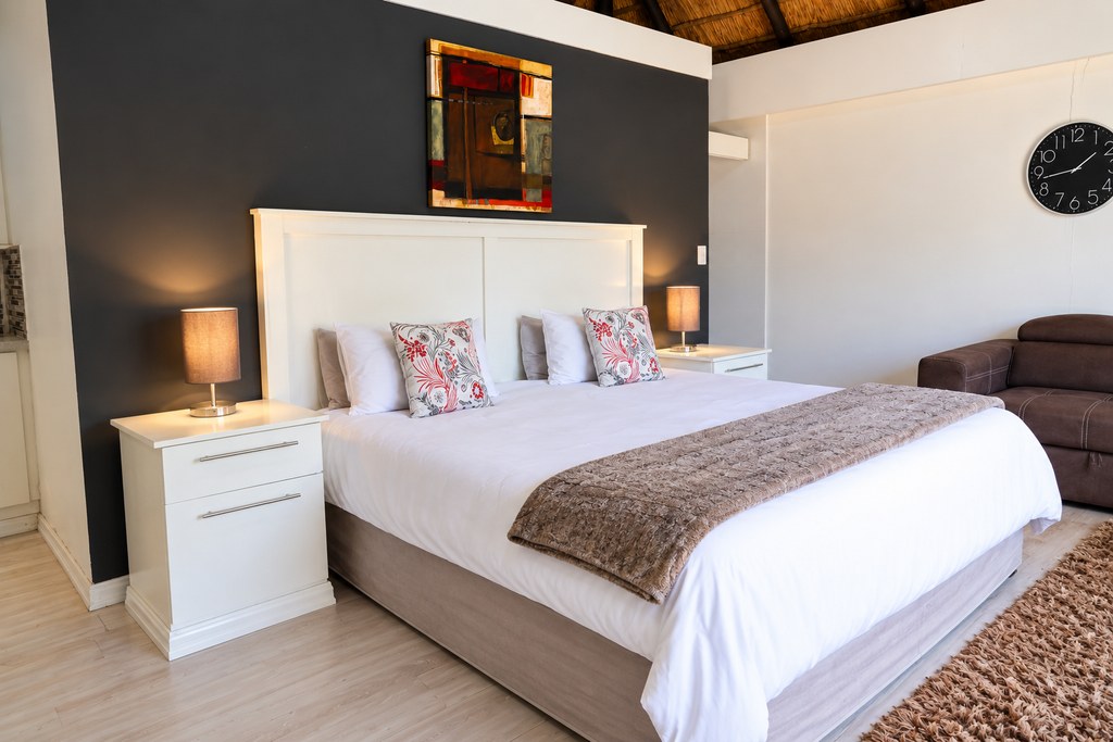 A king bed with bedside lamps against a charcoal feature wall in a Sandstone Room.