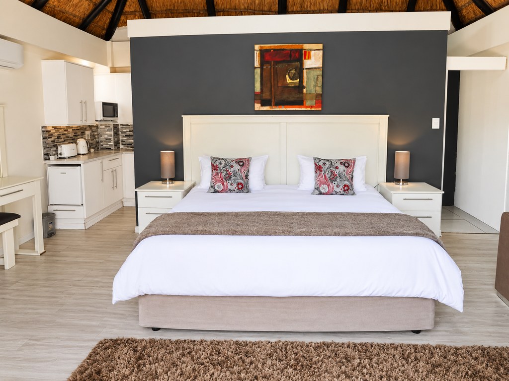 A Sandstone Room with a king bed against a charcoal feature wall and a corner couch alongside.