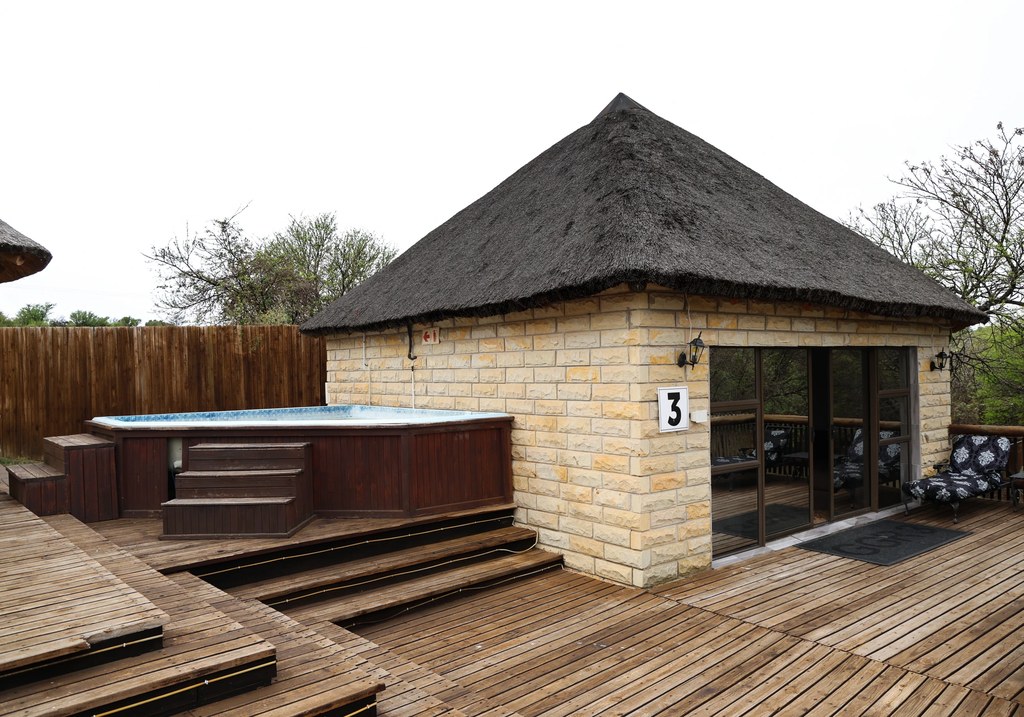 A sandstone unit with a thatched roof beside its timber deck, surrounded by bushveld.