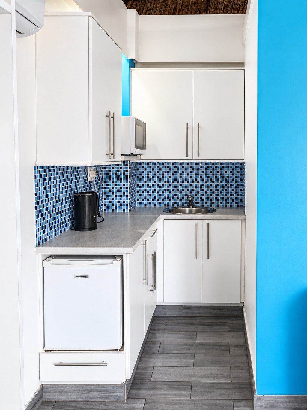 The self-catering kitchenette of a Sandstone Room, with a blue mosaic splashback, microwave, kettle and bar fridge.