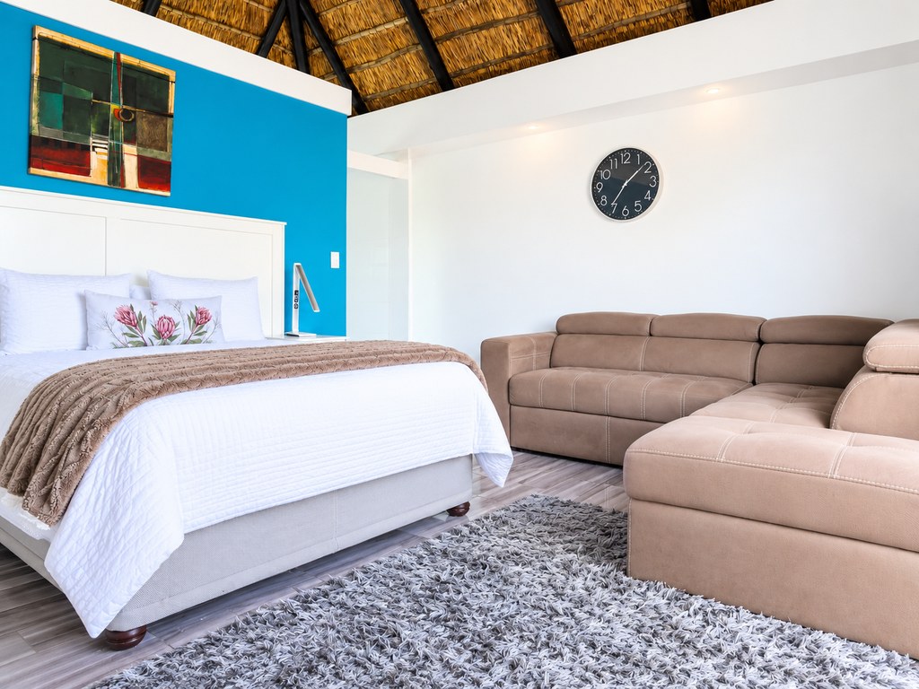 The seating area of a Sandstone Room, with a large corner couch beside the bed under the thatched roof.