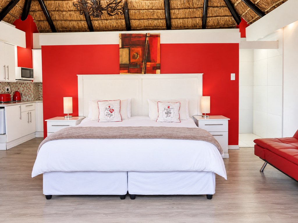 A Sandstone Room with a king bed against a red feature wall and a red couch alongside.