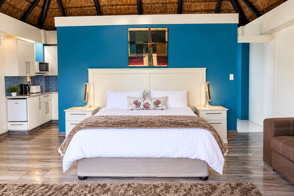 A self-catering Sandstone Room with a king bed against a turquoise feature wall and the kitchenette alongside.