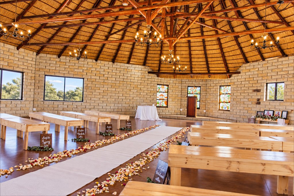 The thatched round hall at Goldfields Game Ranch set for a ceremony, with timber benches either side of a petal-strewn aisle.