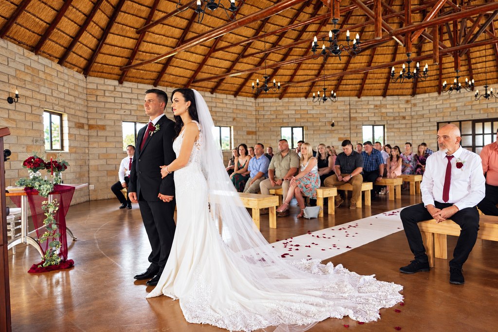 The thatched ceremony hall seen from the rear, with timber benches and a petal-strewn aisle.