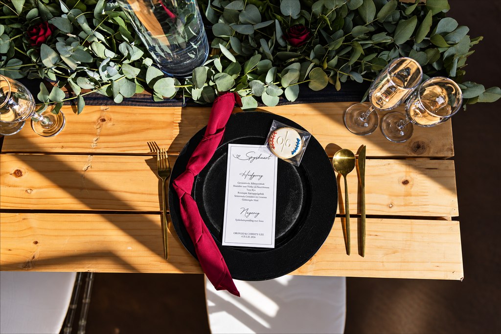 A place setting dressed with eucalyptus, a burgundy napkin and a printed menu card.