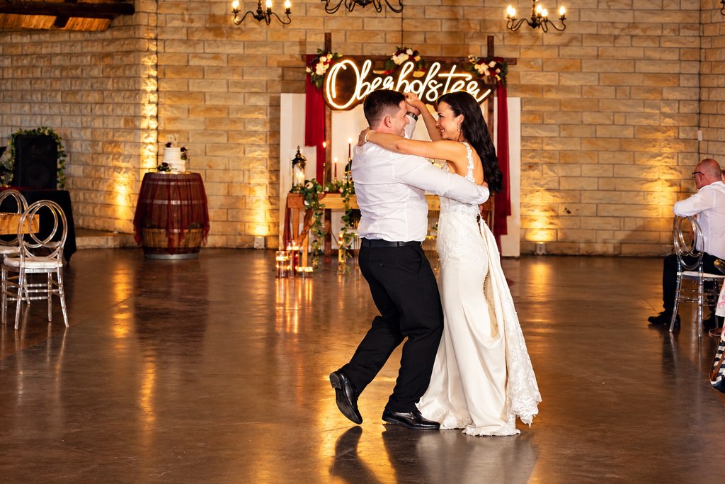 The first dance on the hall floor beneath the illuminated reception backdrop.