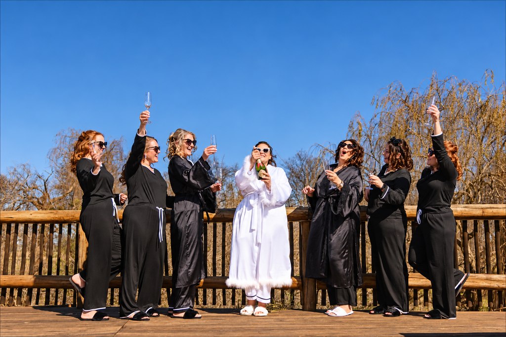 The bride and her bridesmaids raising champagne glasses on the timber deck.