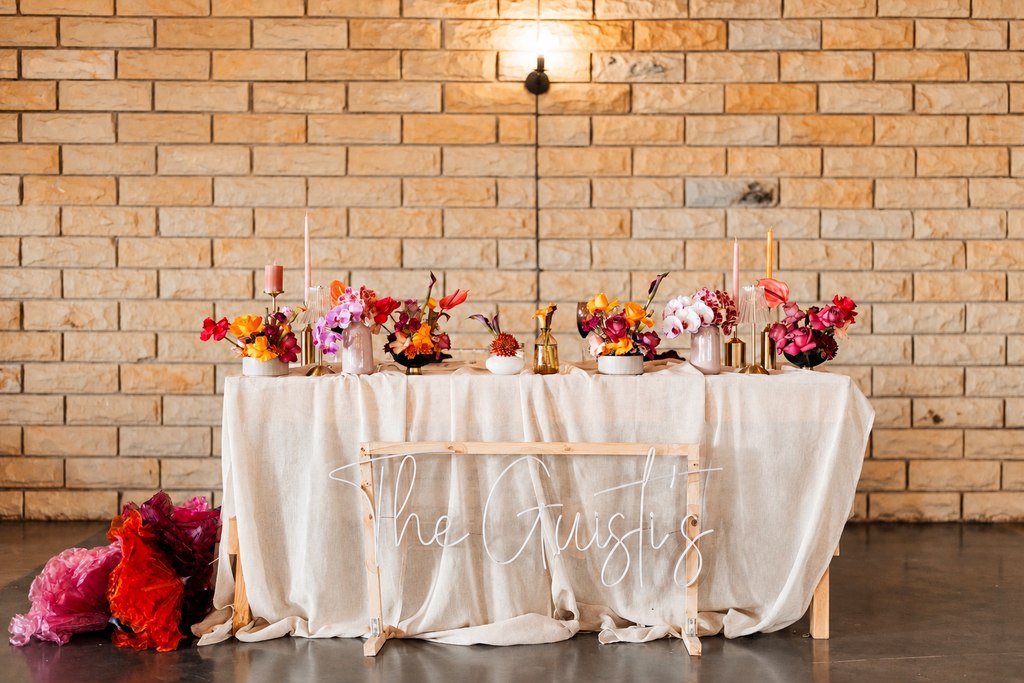 A draped welcome table with floral arrangements against the sandstone wall.