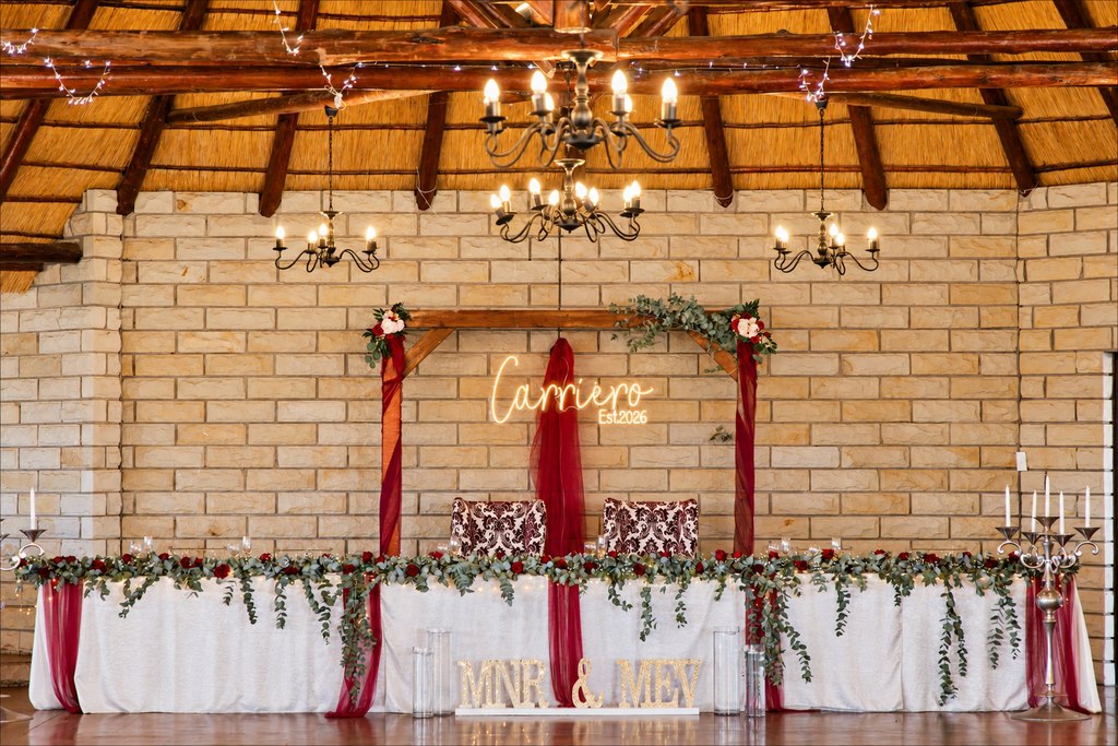 A burgundy-draped head table with a eucalyptus garland and standing lettering.