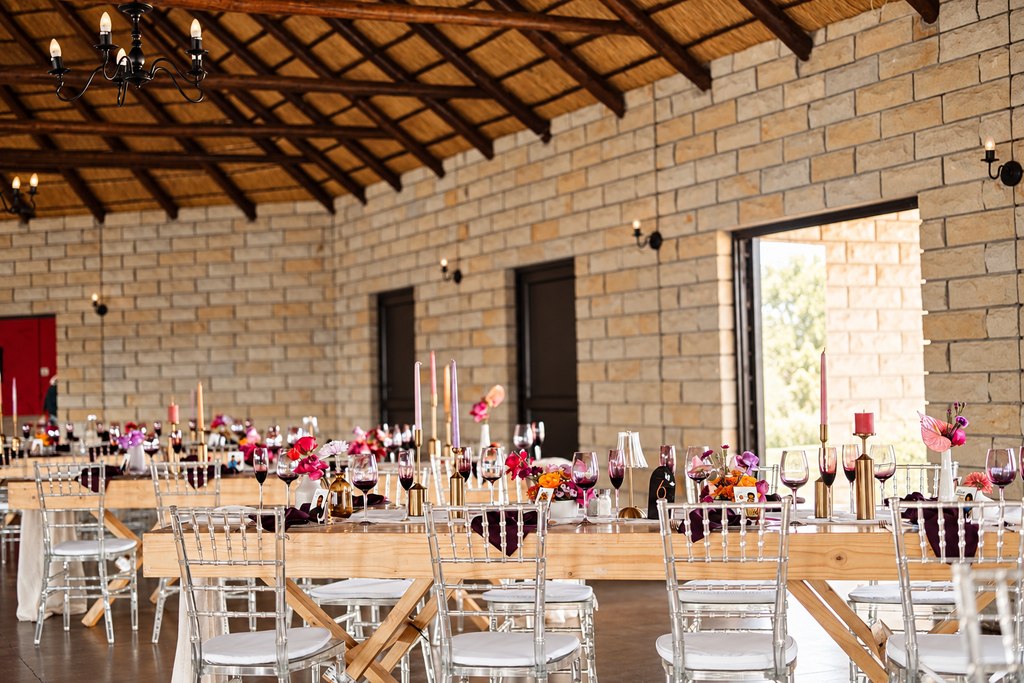 The banquet hall set with long timber tables and clear chairs under thatch.