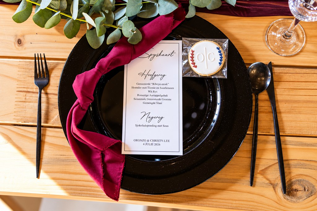 An overhead place setting with a black charger, burgundy napkin and menu card.