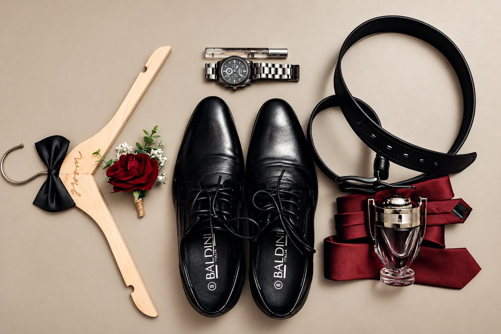 The groom's shoes, bow tie, watch, belt, tie and boutonnière laid out together.