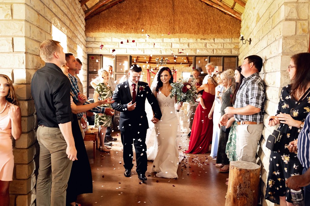 Guests showering a bride and groom with petals as they walk out of the sandstone function hall at Goldfields Game Ranch.