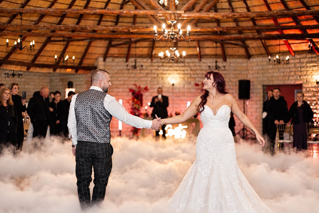 A bride and groom holding hands for their first dance amid low dry-ice cloud in the thatched Goldfields function hall.