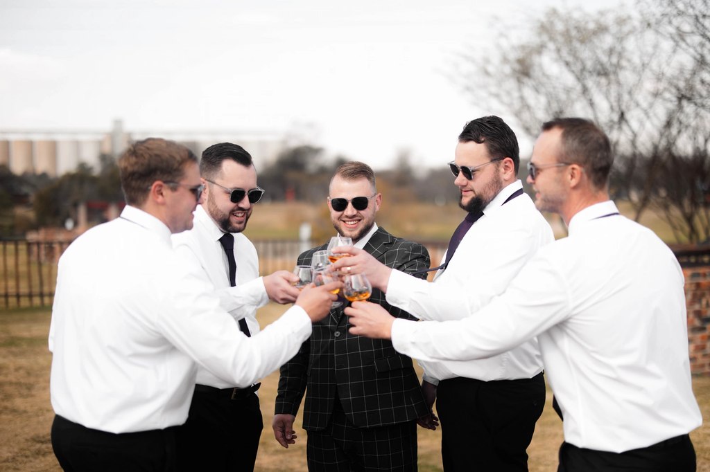 The groom and his groomsmen raising whisky glasses together on the lawn at Goldfields Game Ranch.