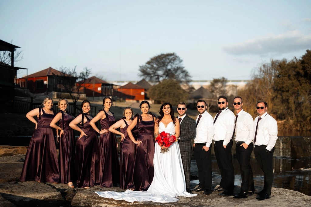 The full bridal party on a rock ledge at golden hour, with chalets and the dam behind at Goldfields Game Ranch.