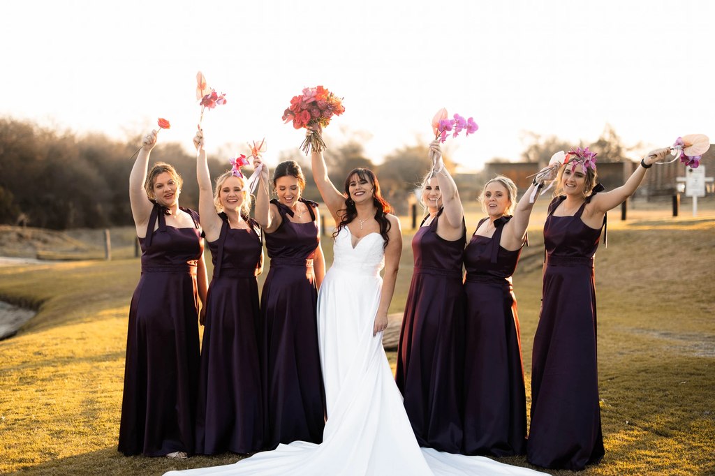 Bridesmaids raising their bouquets around the bride in golden grassland at Goldfields Game Ranch.
