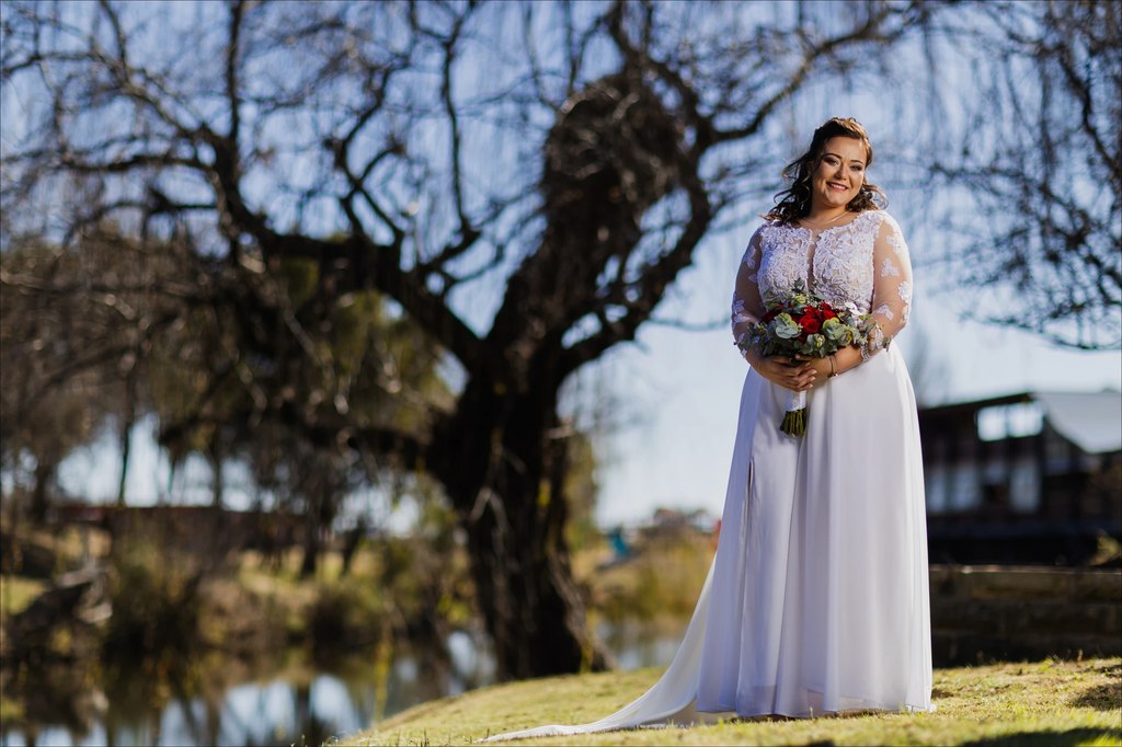 A bride standing beside the dam beneath a bare willow at Goldfields Game Ranch.