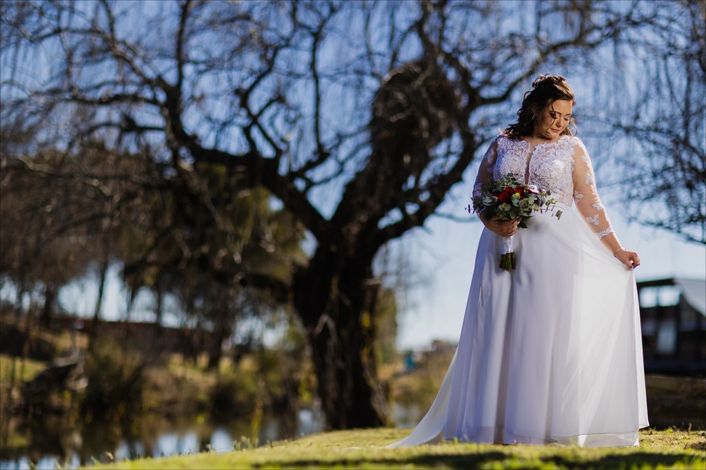 A bride lifting her skirt as she walks beside the dam at Goldfields Game Ranch.