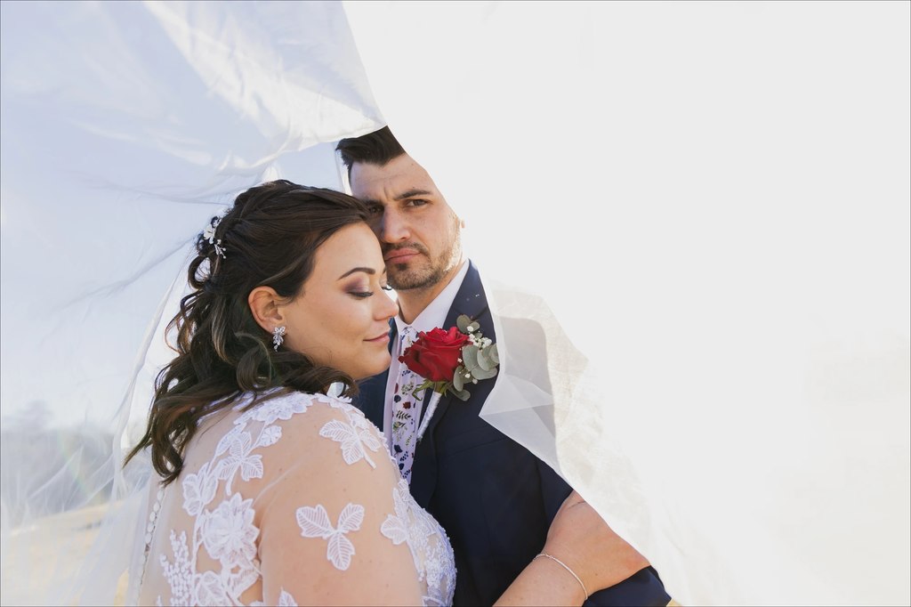 A bride and groom framed by her veil in bright backlight.
