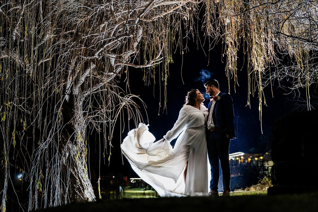 A bride sweeping her dress beneath the illuminated willow canopy at night at Goldfields Game Ranch.
