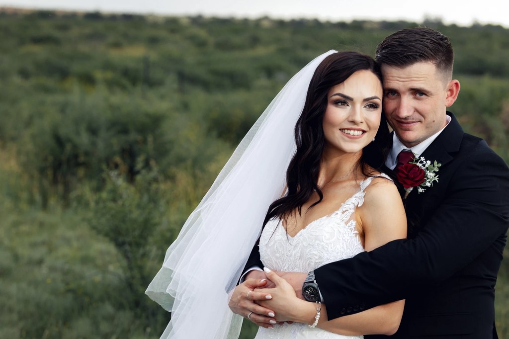 A groom holding the bride from behind against dense green bush in the open Free State landscape.