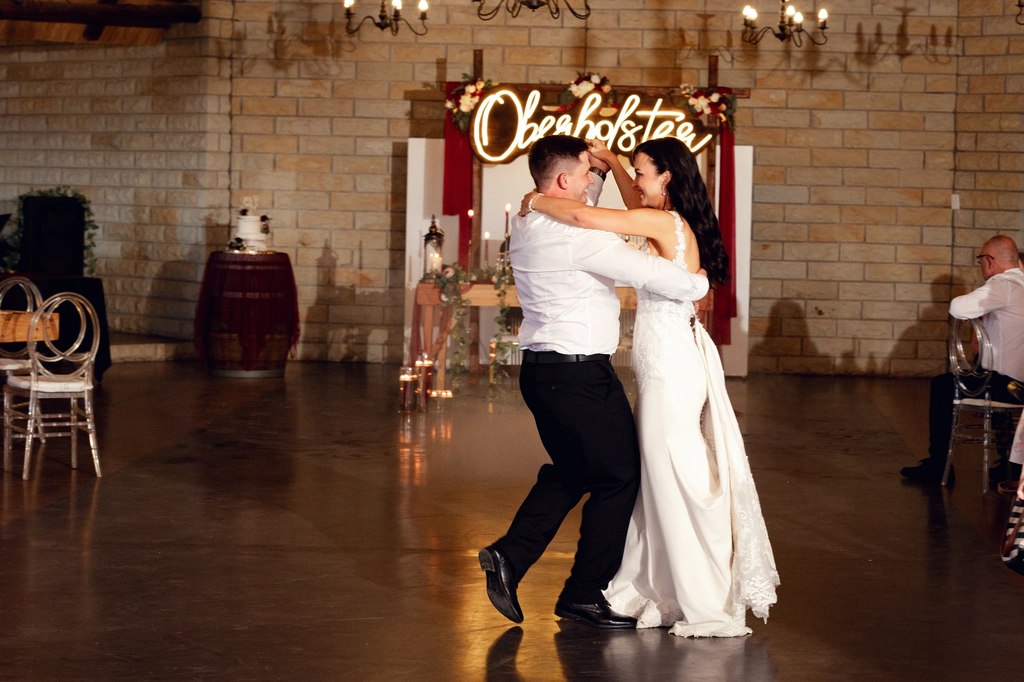 A bride and groom close together during their first dance, the cake table behind them.