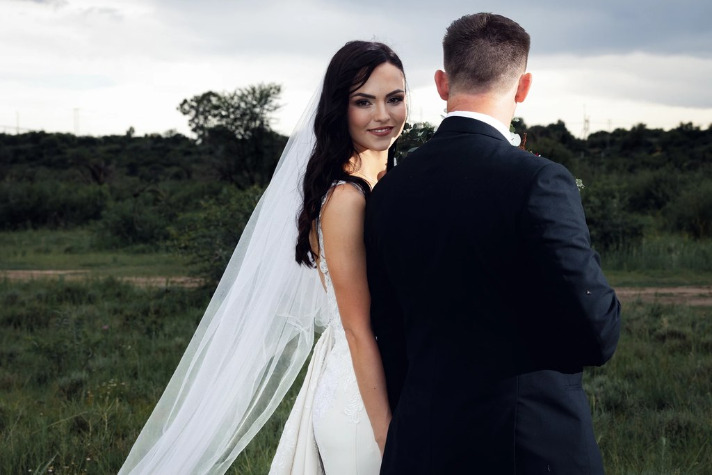 A bride glancing back over her shoulder while standing with the groom in grassland in the open Free State landscape.