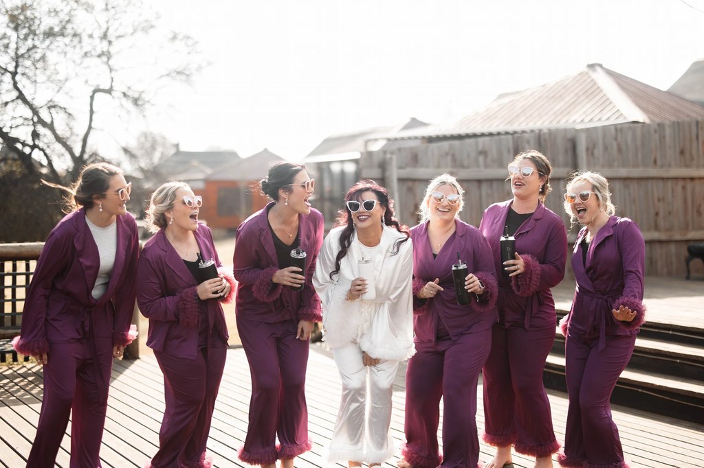 The bride and her bridesmaids in plum pyjamas walking together on the timber deck at Goldfields Game Ranch.