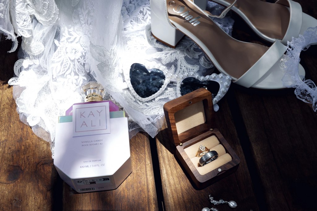The bride's rings in a wooden box beside her shoes, veil lace and fragrance.